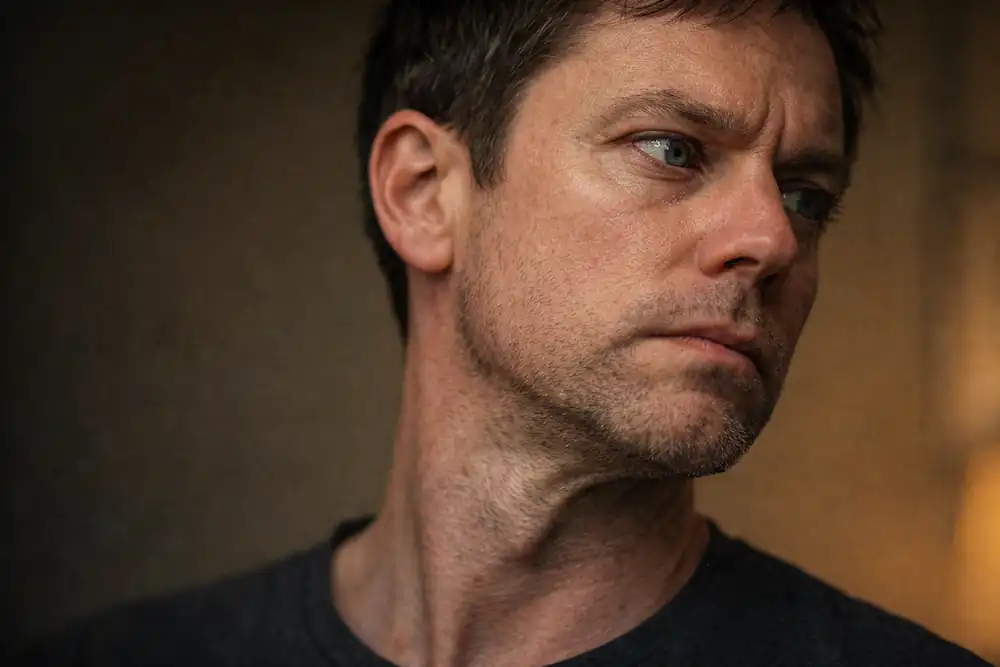 A raw portrait of a person looking out a window with subtle neck tension and visible skin vellus hair, reflecting on emotional healing.