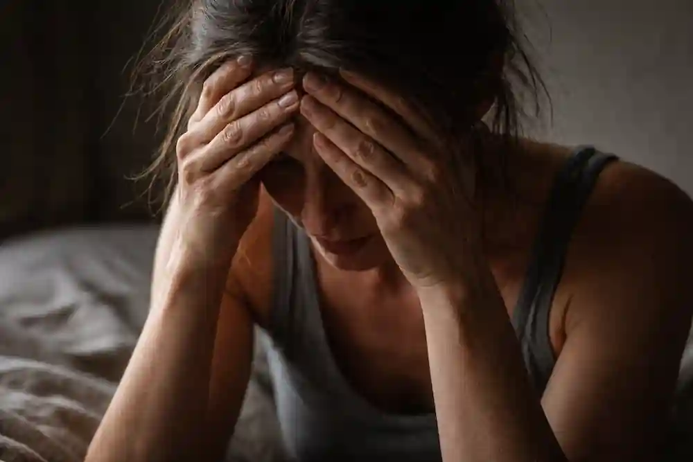 A candid, grainy photograph of a woman sitting with her head in her hands, showing the raw emotion of identifying internal manifestation blocks.