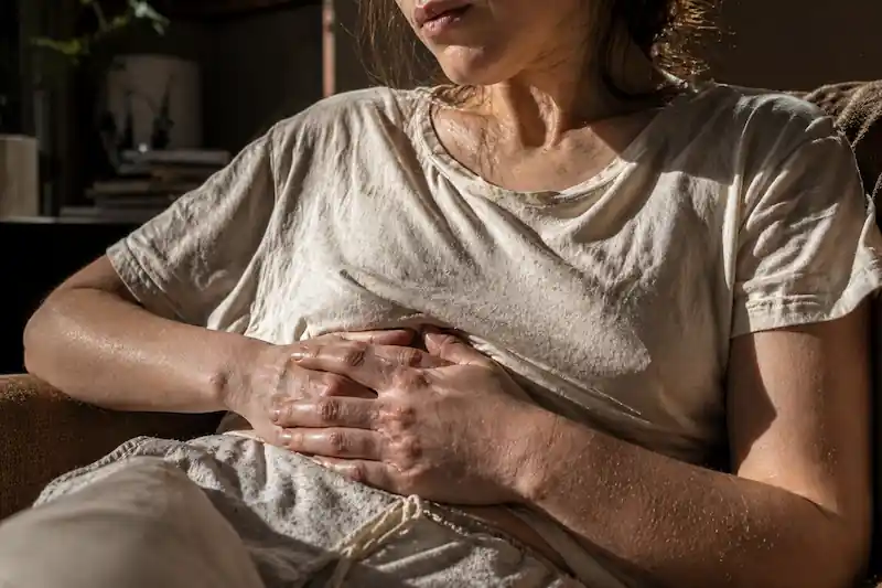 digestive-anxiety.jpg Raw candid photo focusing on a woman's torso, hands clasped over her stomach showing natural skin folds and texture, processing digestive knots during the Full Moon in Scorpio May 1st 2026