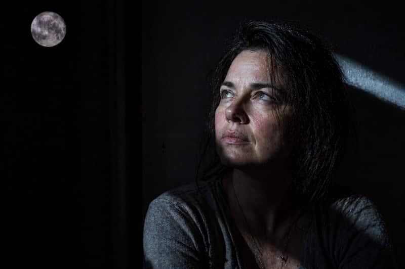 A dark, raw image of a woman performing a Scorpio wealth activation shadow audit under a silver moon.
