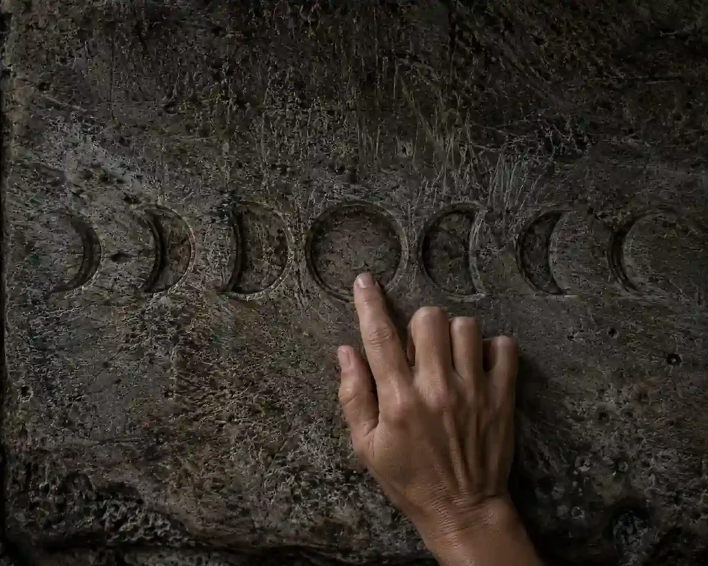 Detailed texture of moon phases on a stone wall with hands touching the red moon cycle phase during a blue moon.