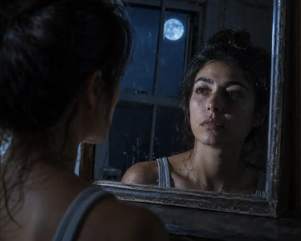 Woman looking into an old mirror reflecting a blue moon, uncovering red moon cycle and birth moon phase meaning.