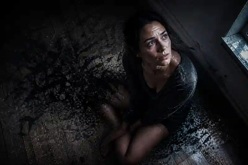 A woman sitting in a dark room with textured wall plaster, experiencing Full Moon symptoms spiritual meaning and the stillness of the Void.